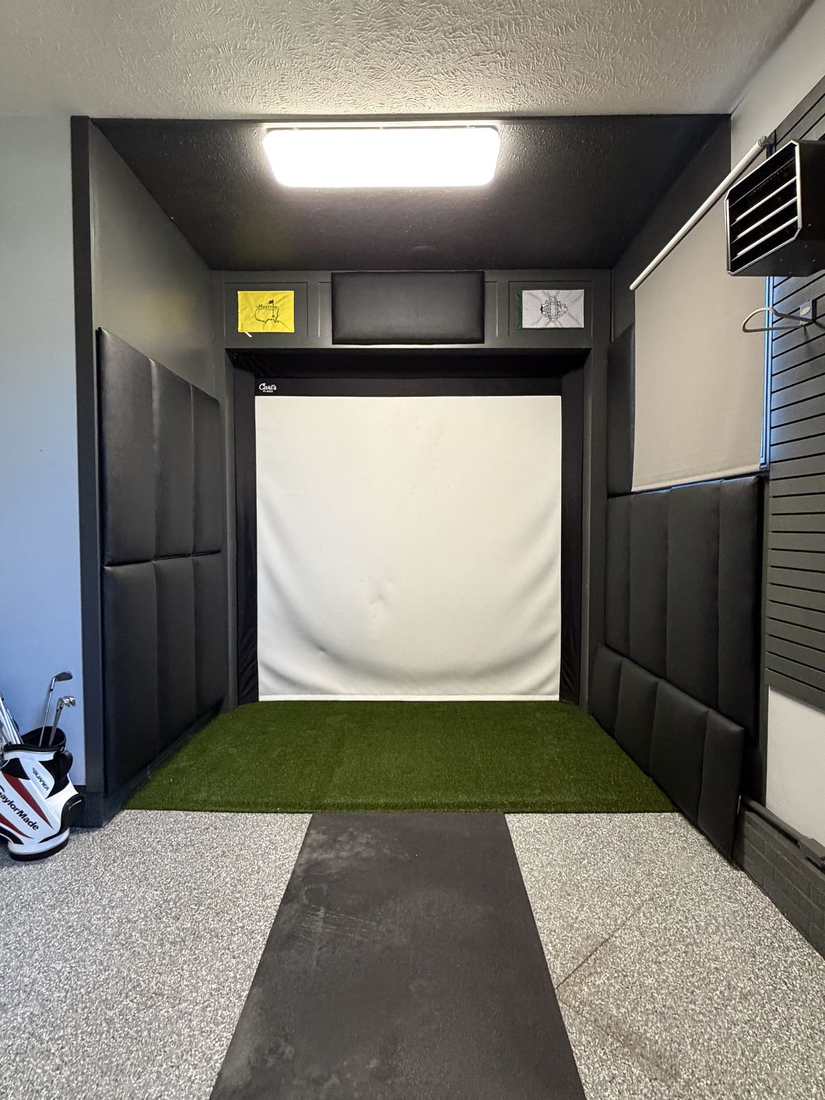 Garage golf simulator with black Shank Pro enclosure, Carl's Place screen, Masters flag